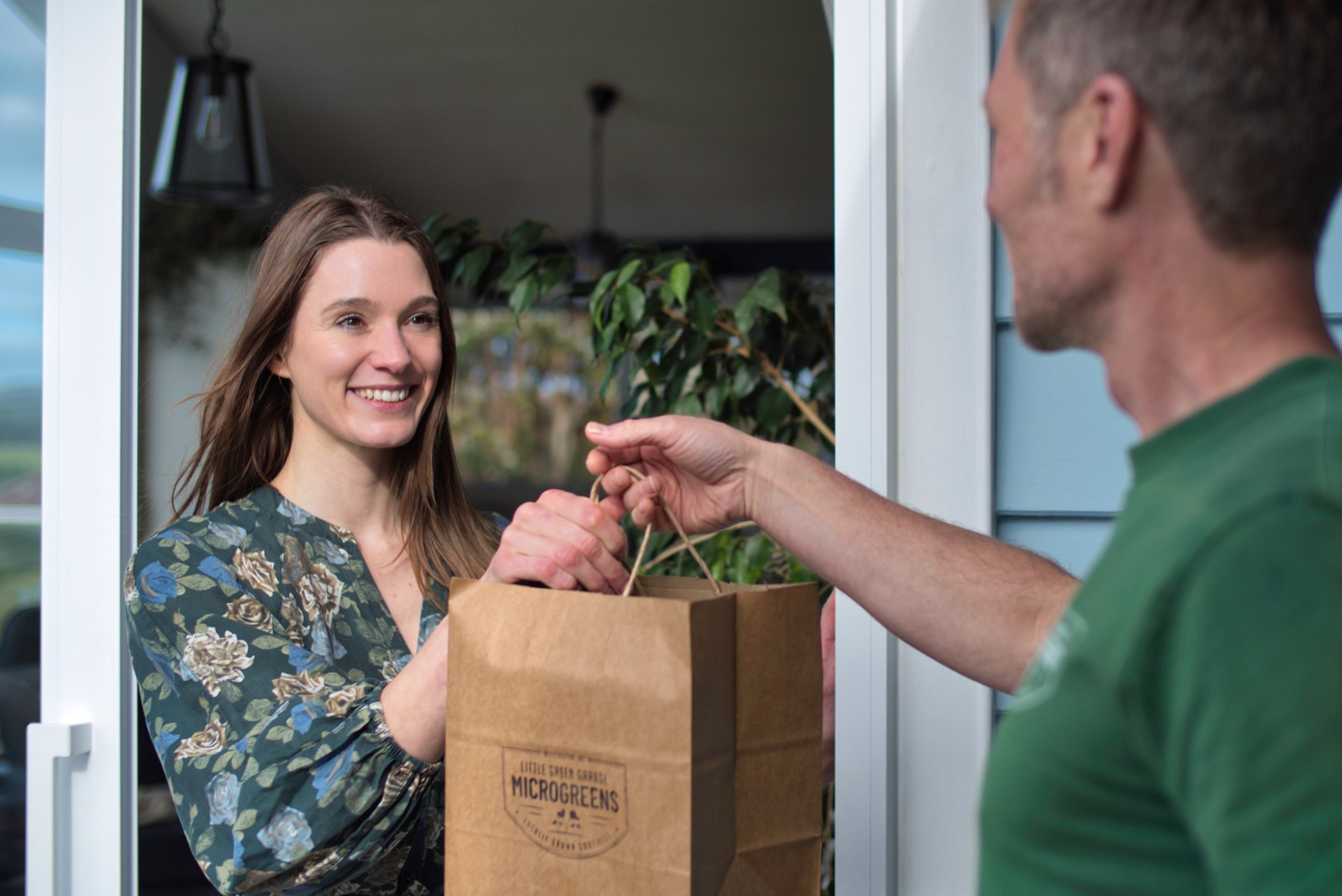 A man handing a bag of microgreens to a woman at her door.