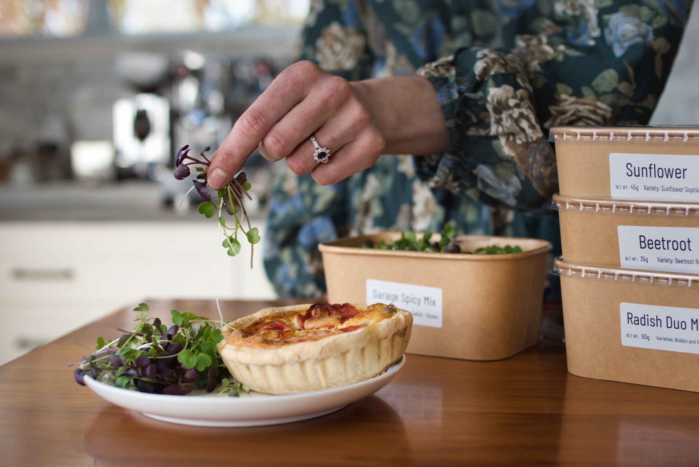 Microgreens being sprinkled on a plate next to a quiche.